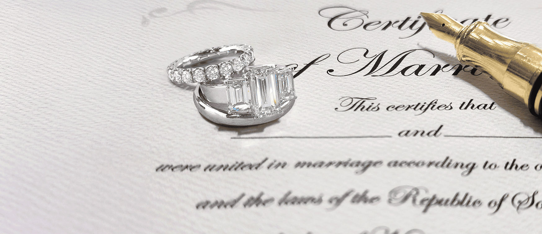 Three-stone Emerald-cut Diamond Engagement Ring and Round Brilliant Diamond Eternity Band Resting on a Marriage Certificate at Mark Solomon Jewellers.