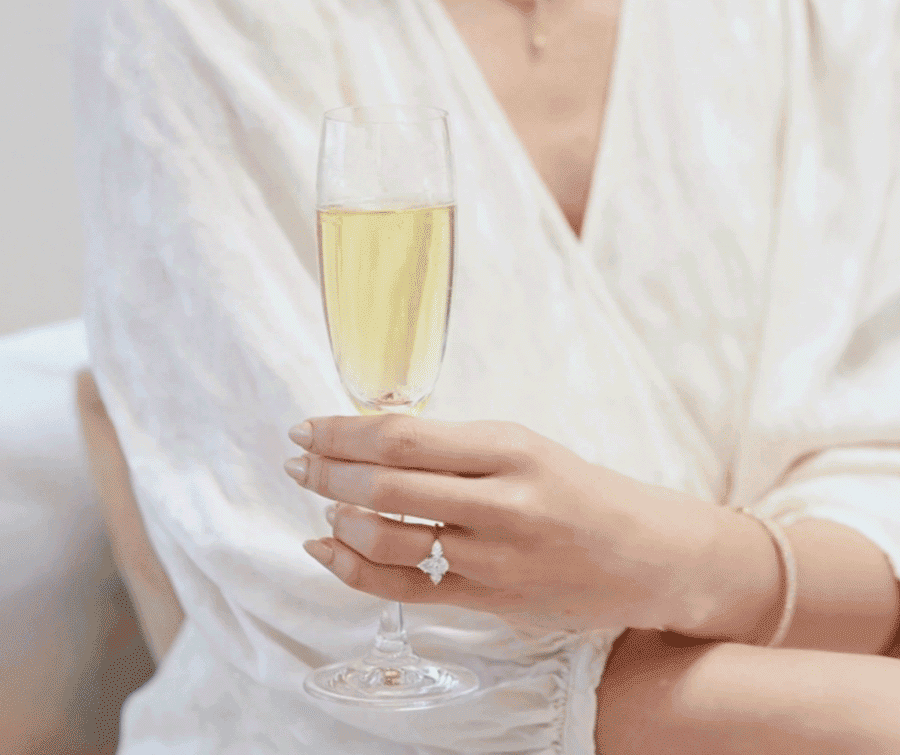 Woman wearing a bespoke diamond engagement ring holding a champagne flute for Mark Solomon Jewellers in Cape Town.