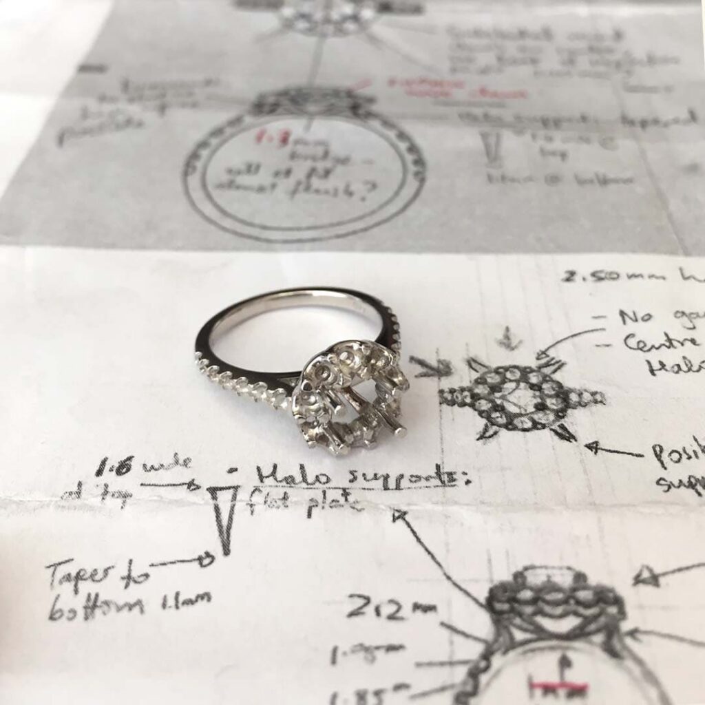 Bespoke Cluster Halo Ring Setting in White Gold Resting on Hand-drawn Technical Jewellery Design Sketches and Measurements.