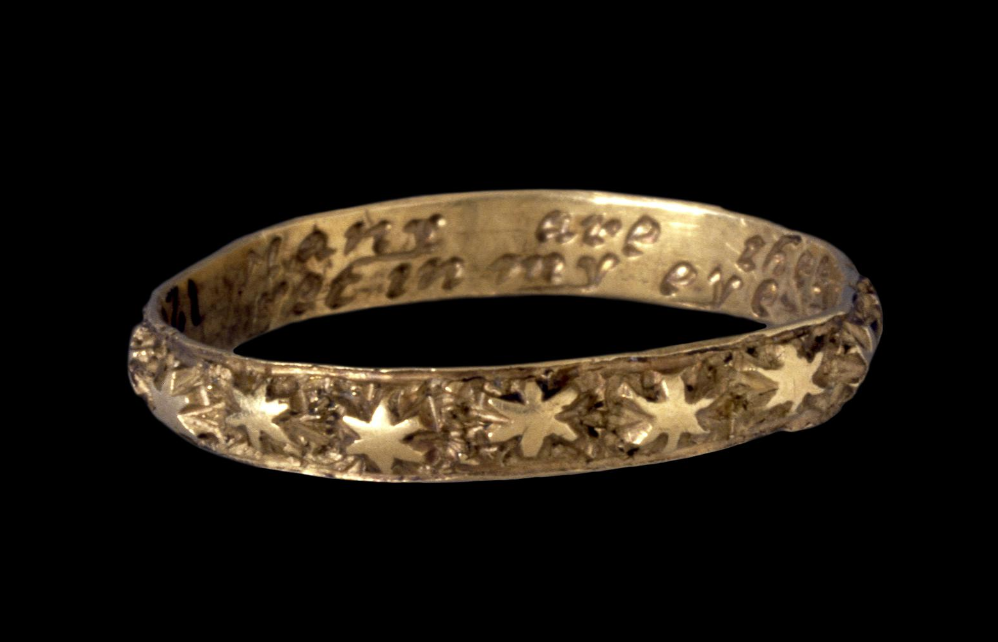 Gold Band Ring with Star-shaped Raised Motifs Along the Outside and Inscriptions Inside on a Black Background.