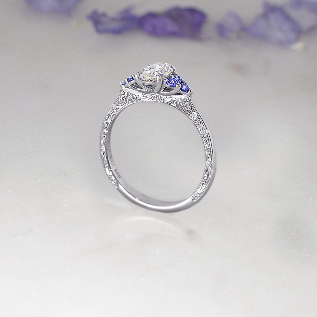 Custom Oval Diamond Ring with Tanzanite Cluster Accents and a Hand-engraved Platinum Band Featuring Scrollwork Detailing.
