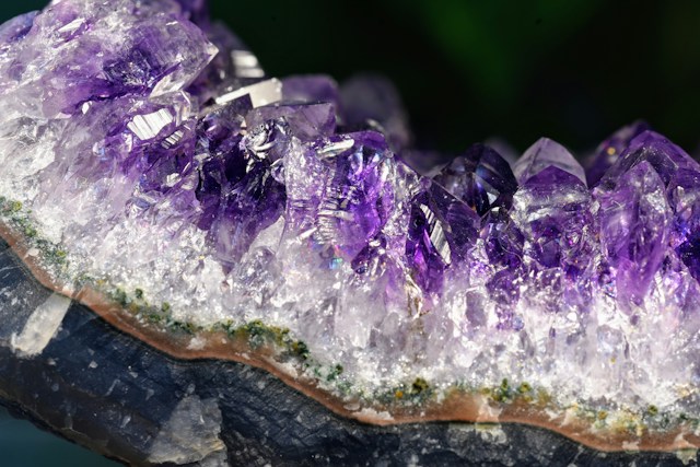 Close-up of Purple Amethyst Crystals Forming a Geode Along a Rock Base, Sparkling Facets Catching Light.