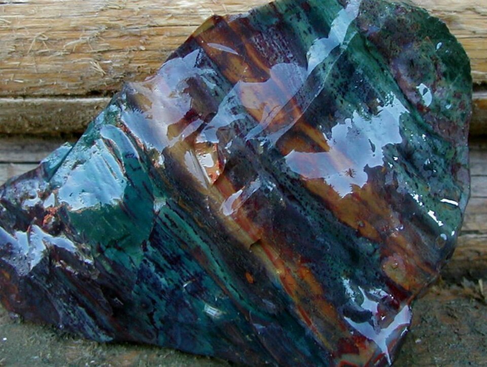 a Large, Irregular, Glassy Rock with Vivid Blue, Green, and Brown Swirls Resting on a Wooden Surface.