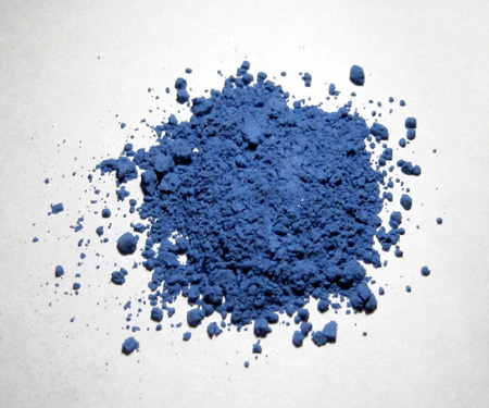 Blue Pigment Powder Scattered in a Circular Pile on a White Surface, with Small Surrounding Specks.