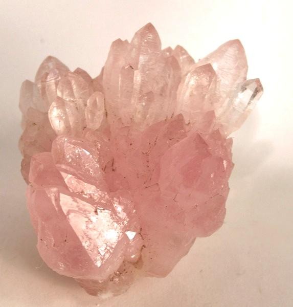 Pink Rose Quartz Crystal Cluster with Pointed Terminations and Translucent Facets on a White Surface.