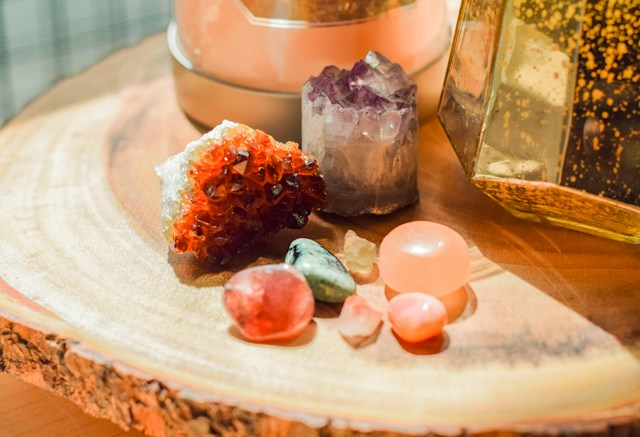 Colorful Crystals and Minerals Arranged on a Wooden Slab with Warm Light and Amber Glass in the Background.