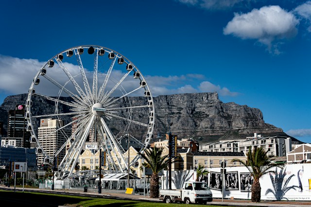 Large White Ferris Wheel Beside a Coastal City with Table Mountain in the Background, Under a Blue Sky.