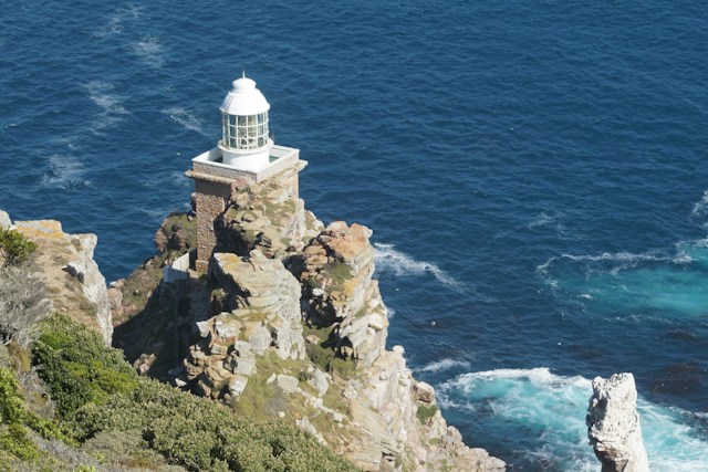 Lighthouse Perched on a Jagged Rocky Cliff Overlooking the Blue Ocean.