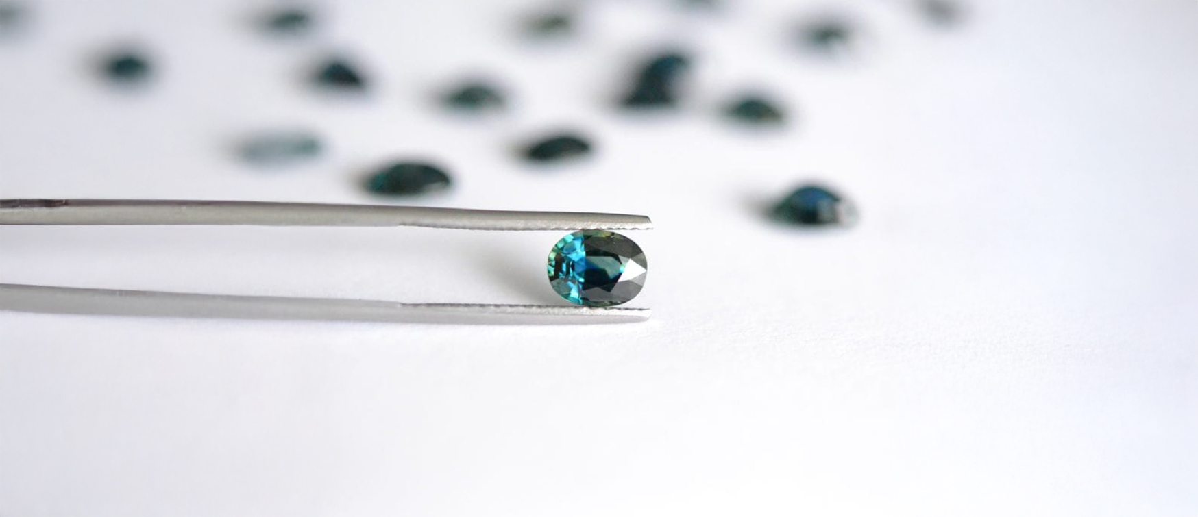 Loose Peacock Sapphire Gemstone – Mark Solomon Jewellers - Mark Solomon Jewellers Loose Peacock Sapphire Gemstone Held by Tweezers with Scattered Stones in Background