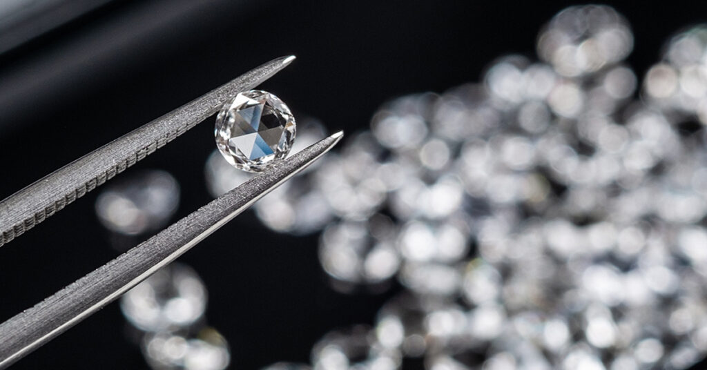 Rose Cut Diamond in Tweezers Mark Solomon Jewellers - Mark Solomon Jewellers Loose Round Rose Cut Diamond Held in Jeweller's Tweezers over a Background of Loose Diamonds at Mark Solomon Jewellery Designers.