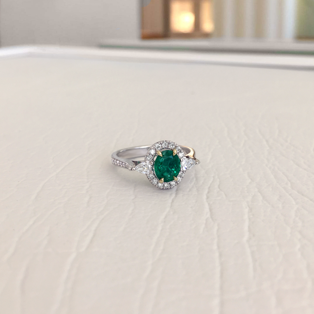 Green gemstone jewellery | An oval emerald flanked by two sparkling pear-shaped diamonds, with a glittering partial halo and a pavé-set band
