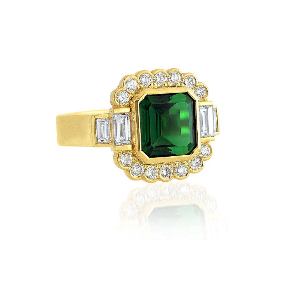 Green Gemstone Jewellery | This art-deco inspired Tourmaline and Baguette Diamond Ring heralds a vivid green tourmaline gemstone (chrome tourmaline totalling 2.70ct with EGL Certification), shouldered by 4 baguette-cut diamonds (baguette-cut diamonds totalling: 0.38ct, F-G colour), with a partial halo of 14 glittering round brilliant cut diamonds (round brilliant diamonds totalling: 0.29ct, VS clarity).

Handcrafted by our Master Goldsmiths on our premises using the highest grade 18ct yellow gold.