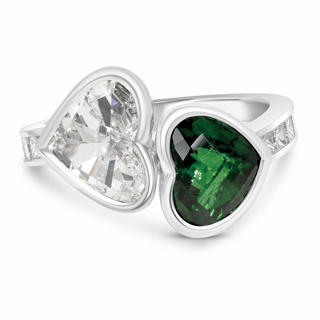 a Unique "toi Et Moi" Ring Featuring Two Heart-shaped Gemstones, a Clear Diamond and a Deep Green Gemstone (likely Emerald or Tourmaline), Bezel-set Side-by-side on a White Gold or Platinum Band with Channel-set Accent Stones.