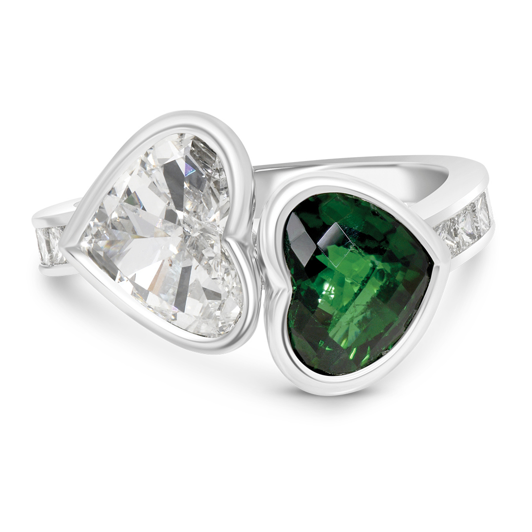 a Unique "toi Et Moi" Ring Featuring Two Heart-shaped Gemstones, a Clear Diamond and a Deep Green Gemstone (likely Emerald or Tourmaline), Bezel-set Side-by-side on a White Gold or Platinum Band with Channel-set Accent Stones.