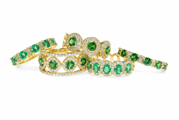 a Beautiful Collection of Yellow Gold Rings Featuring Green Gemstones and White Diamonds. the Rings Have Various Designs Including a Full Circle Eternity Band, an Oval Cluster Ring, and a Ring with Pave-set Diamond Halos and Circular Green Gemstones.