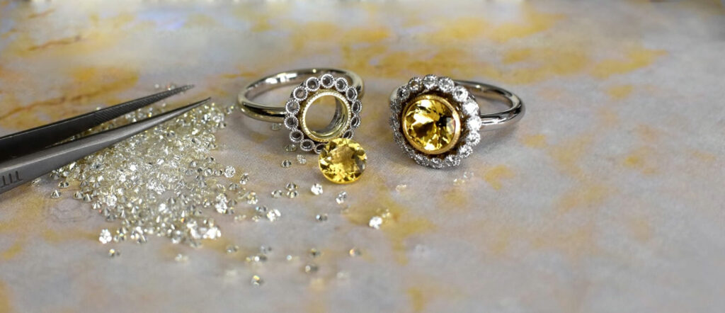 Two Rings Featuring Yellow Gemstones Shown Alongside Loose Diamonds and Jeweller’s Tweezers on a Softly Textured Surface, Highlighting the Jewellery-making Process.