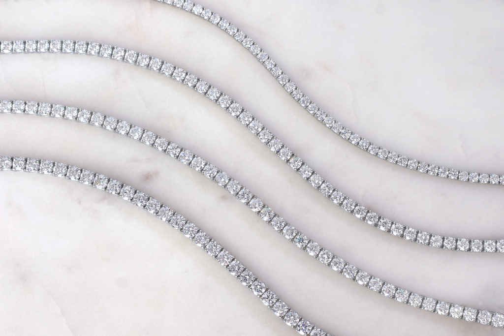 Diamond Tennis Bracelet Collection - Mark Solomon Jewellers Several Diamond Tennis Bracelets Arranged in Soft Curves on a Light Marble Surface.