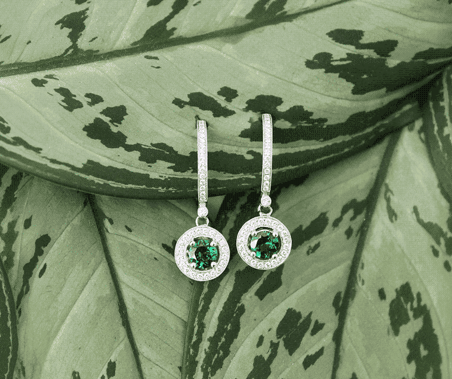 Platinum or 18ct white gold green gemstone drop earrings with micro-pavé halos resting on lush green leaves for Mark Solomon Jewellers.