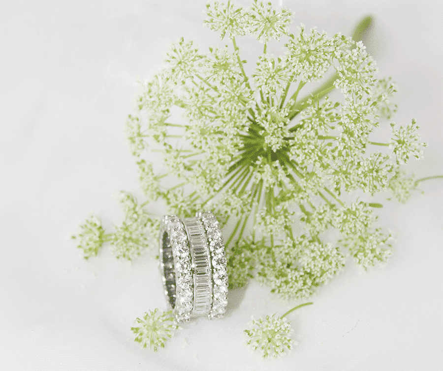 Wide platinum baguette and round brilliant diamond ring resting beside a delicate white floral stem at Mark Solomon Jewellers in Cape Town.